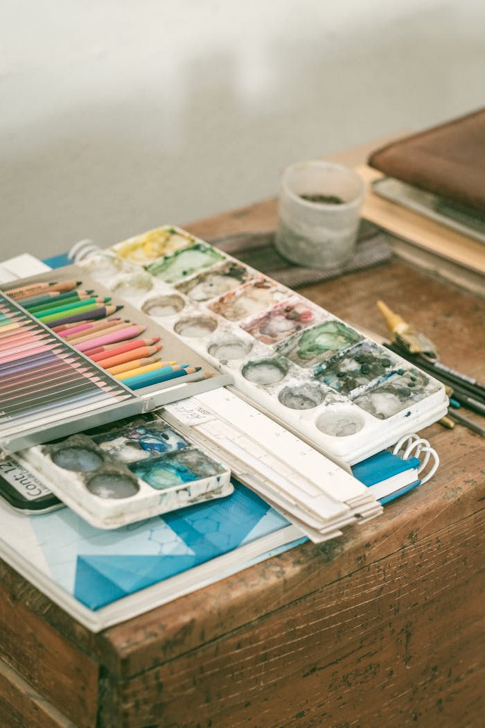 A collection of colorful art supplies including paints, pencils, and brushes on a wooden desk.