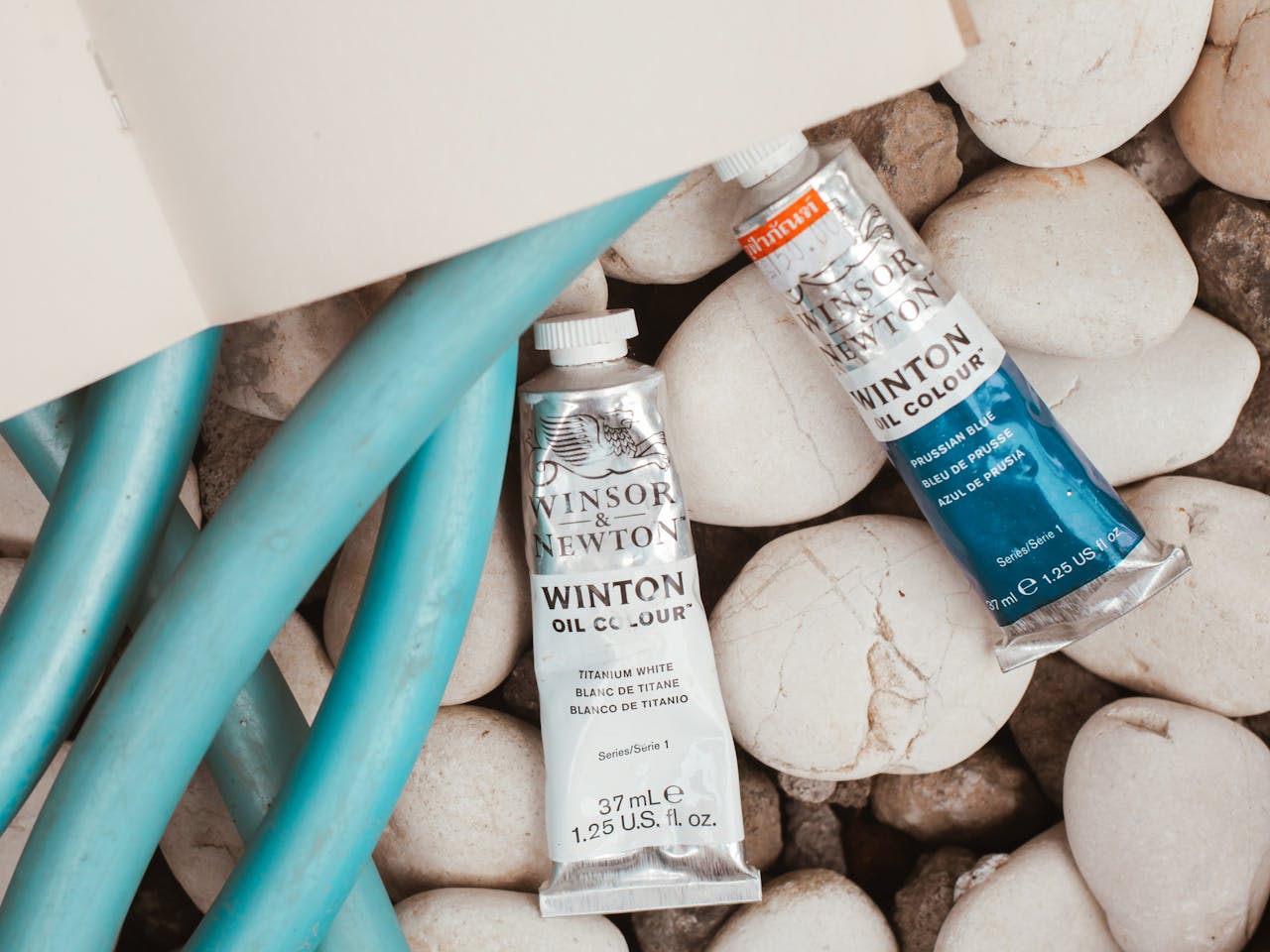 about-us-02 Artistic composition featuring Winsor & Newton oil paint tubes on pebbles.